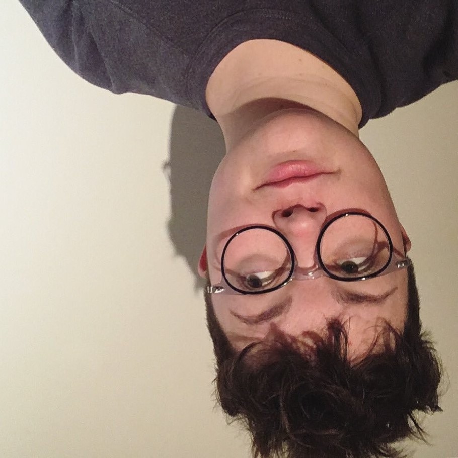 upside down selfie of katie, a white nonbinary person with curly brown hair and round glasses